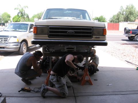 1990 Ford Bronco - Mechanics are working on the suspension of a lifted Ford Bronco, with another Ford truck visible in the background.