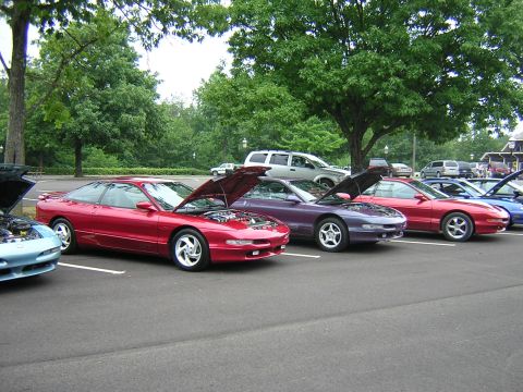1995 Ford Probe - A line of Ford Probes, including a red one with its hood open, are parked in a lot on a sunny day.