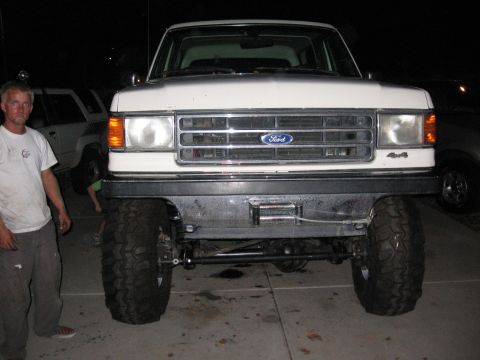 1990 Ford Bronco - A white Ford truck with oversized tires and a winch is parked in front of another vehicle.