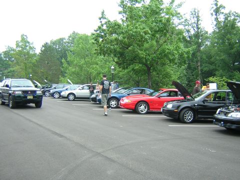 1995 Ford Probe - A red sports car is parked in a lot alongside other cars, some with hoods open.
