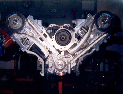 1992 Ford Crown Victoria - Front view of a partially assembled aluminum V8 short block on an engine stand with the timing covers off, showing dual overhead-cam chains…