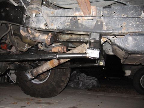 1990 Ford Bronco - Undercarriage view of a vehicle's suspension and exhaust system, with a prominent tire visible. Text reads SUPERMOTORS.NET.