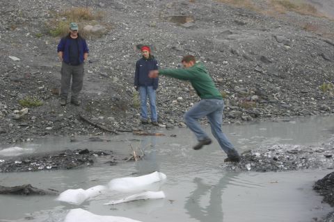 2003 Jeep TJ - Three people navigate a rocky, icy terrain with a shallow, murky stream.