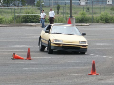 2001 Mercury Grand Marquis - A yellow hatchback is shown on a paved lot with traffic cones, possibly during a driving event.