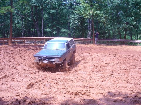 1996 Ford Bronco - A Ford Bronco navigates a muddy terrain with trees in the background.