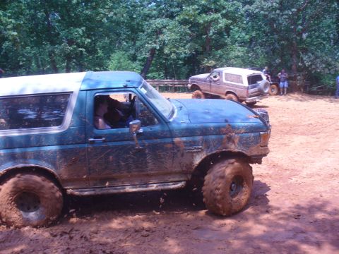 1996 Ford Bronco - Two Ford Broncos navigating a muddy off-road course on a sunny day.