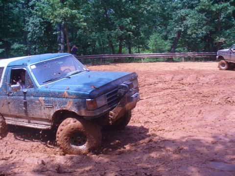 1996 Ford Bronco - A blue Ford Bronco is stuck in deep mud, with another vehicle visible in the background.