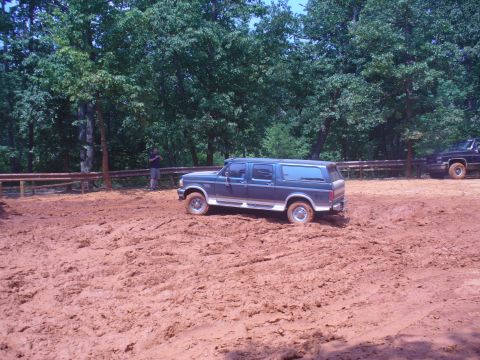 1996 Ford Bronco - A 1996 Ford Bronco navigates a muddy terrain, with another vehicle visible in the background.