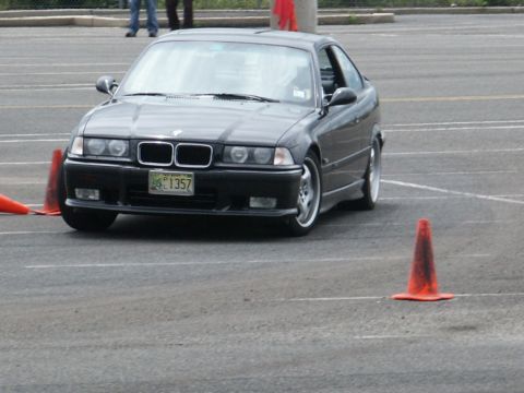 2001 Mercury Grand Marquis - A black BMW E36 coupe navigates a course marked by orange traffic cones on a paved surface.