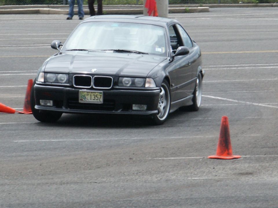 Black BMW E36 coupe with a license plate reading 'BG 1357' driving around orange cones on a paved lot