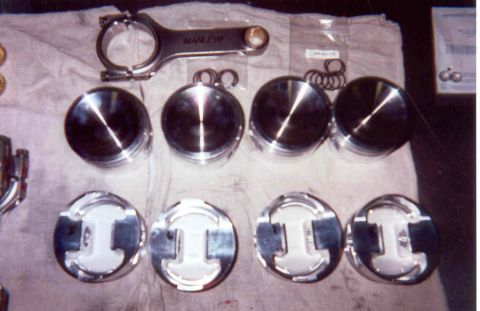 1992 Ford Crown Victoria - Engine rebuild parts laid out on a light cloth: four polished forged pistons shown crown-up in the top row with their ring sets, four more…