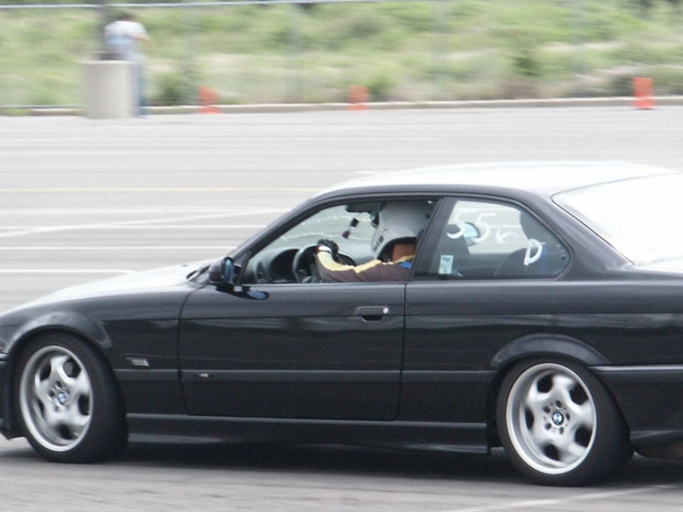 Black coupe with racing drivers wearing helmets, side view