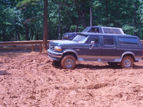 1996 Ford Bronco - Two SUVs navigate a muddy terrain with trees in the background.