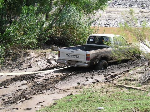 1993 Ford Bronco - A white Toyota pickup truck is stuck in thick mud, with a tow strap attached to its rear bumper.