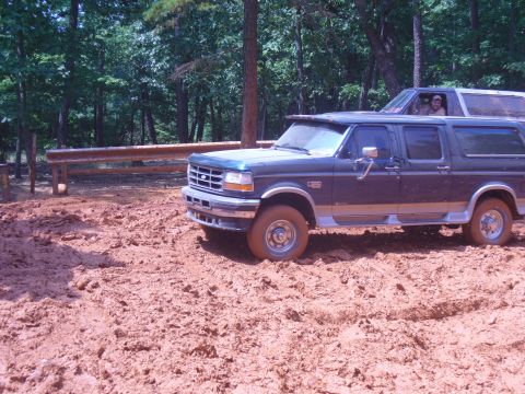 1996 Ford Bronco - A dark blue 1995 Ford F-Series SUV navigates a muddy terrain, with another vehicle visible behind it.