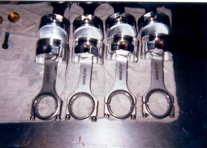 Four forged pistons on polished Manley H-beam connecting rods on a bench