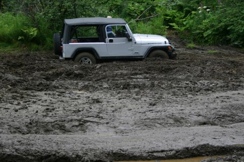 2003 Jeep TJ - A 2003 Jeep TJ is stuck in thick mud, with a tow rope visible.