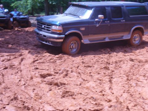 1996 Ford Bronco - A Ford Bronco navigates a muddy terrain, with ATVs visible in the background.