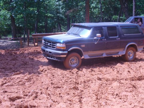 1996 Ford Bronco - A dark blue SUV navigates a muddy terrain, with another vehicle visible behind it.