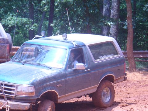 1996 Ford Bronco - A 1996 Ford Bronco is seen off-roading in a wooded area with another vehicle nearby.