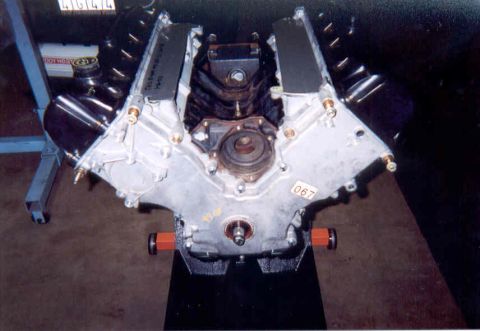 1992 Ford Crown Victoria - Assembled aluminum V8 long block standing on a wood plank on the shop floor, viewed head-on down the valley with the timing cover, crank sn…