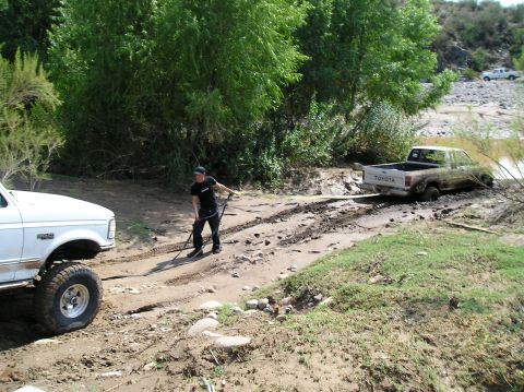 1993 Ford Bronco - A man uses a tow strap to pull a stuck Toyota pickup truck from a muddy ditch with a Ford F-Series truck.