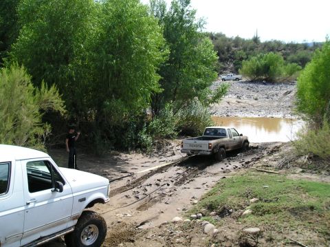1993 Ford Bronco - Two trucks are stuck in the mud, one being pulled by the other. A person stands nearby.