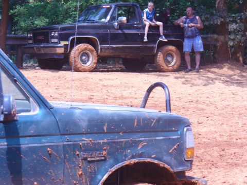 1996 Ford Bronco - A green Bronco with a roll bar is in the foreground, while a black GMC pickup truck is parked behind it.