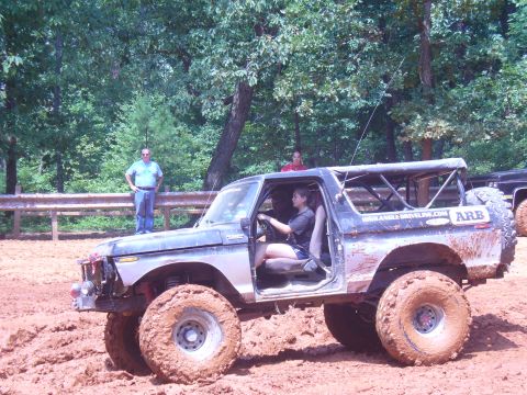 1996 Ford Bronco - A heavily modified Ford Bronco navigates a muddy off-road course with spectators watching.