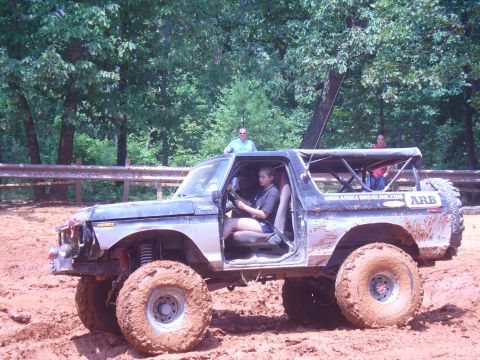1996 Ford Bronco - This modified SUV is navigating a muddy terrain with several people inside.