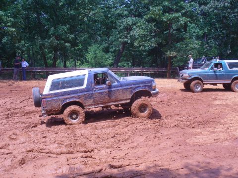1996 Ford Bronco - Two Ford Broncos navigate a muddy off-road course during an event.