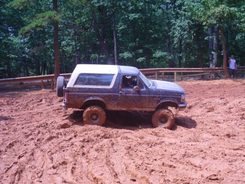 1996 Ford Bronco - Ford Bronco navigating a muddy off-road trail with its tires deep in the muck.