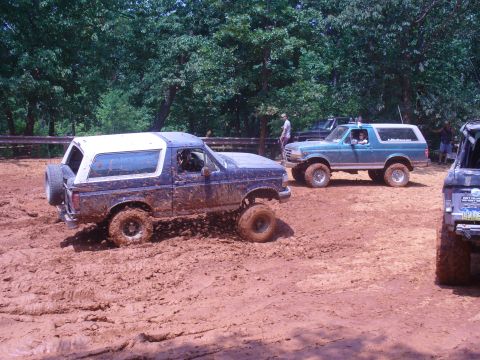 1996 Ford Bronco - Several Ford Broncos navigate a muddy off-road course on a sunny day.
