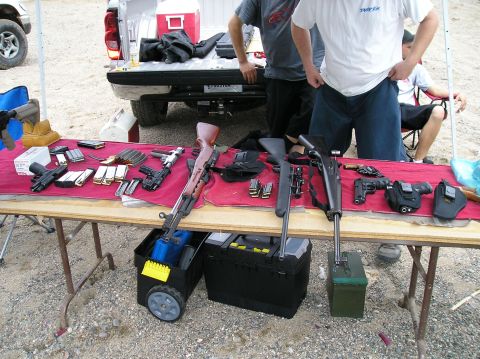 1993 Ford Bronco - A table displays various firearms and ammunition, with a pickup truck and individuals present in the outdoor setting.