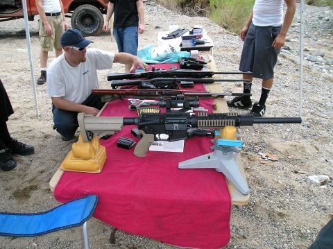1993 Ford Bronco - A variety of firearms are displayed on a table outdoors, with several individuals present.