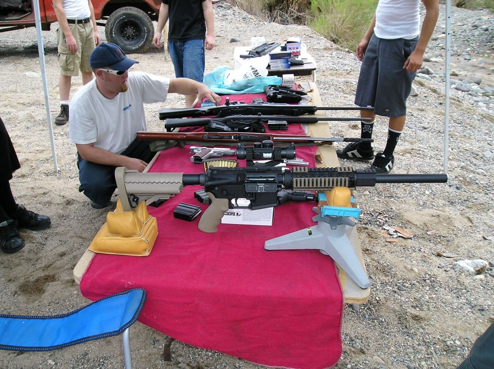 Rifles and pistols laid out on a red-covered table at an outdoor shooting range
