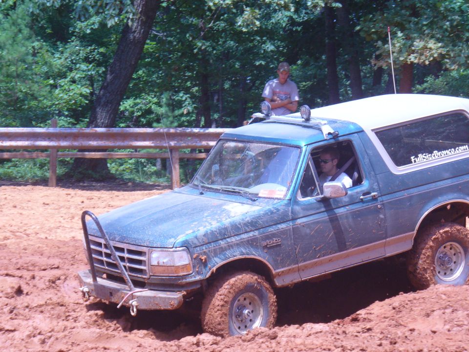 Green 1996 Ford Bronco stuck in mud with a person standing on the roof