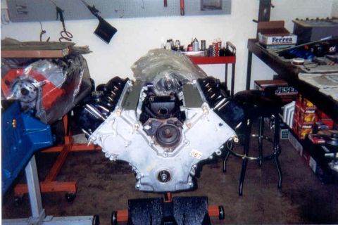 1992 Ford Crown Victoria - Front view of an assembled V8 short block on an engine stand in a home workshop, with bare aluminum timing cover, exposed cam gear area and…