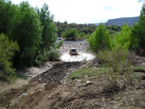 1993 Ford Bronco - A white SUV navigates a challenging muddy terrain, with another vehicle visible in the distance.