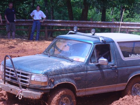 1996 Ford Bronco - A green 1996 Ford Bronco navigates a muddy off-road course with two people watching.