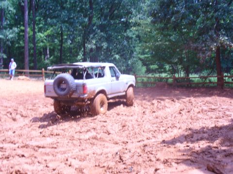 1996 Ford Bronco - A white Ford Bronco navigates a muddy terrain with trees in the background.
