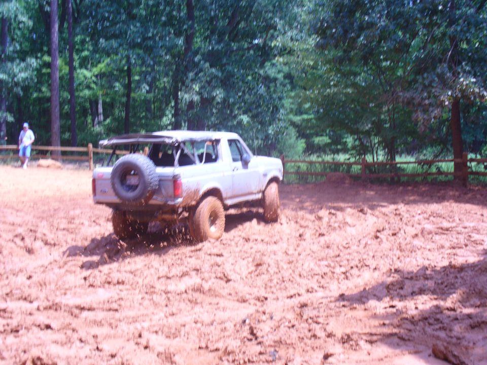 White Ford Bronco with spare tire on rear, driving through mud
