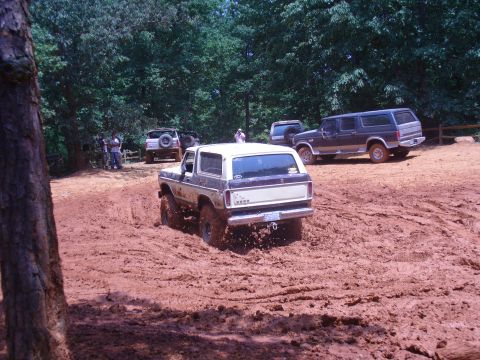 1996 Ford Bronco - Several SUVs navigate a muddy off-road course on a sunny day.