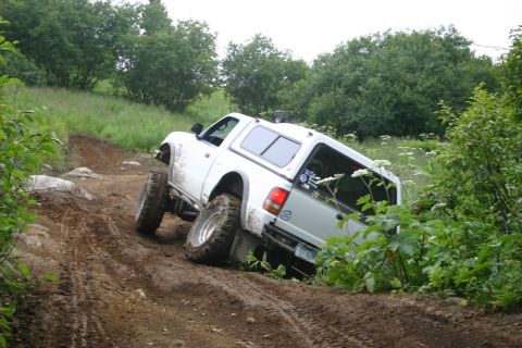 2003 Jeep TJ - Off-road pickup truck climbing a steep, muddy incline surrounded by dense vegetation.
