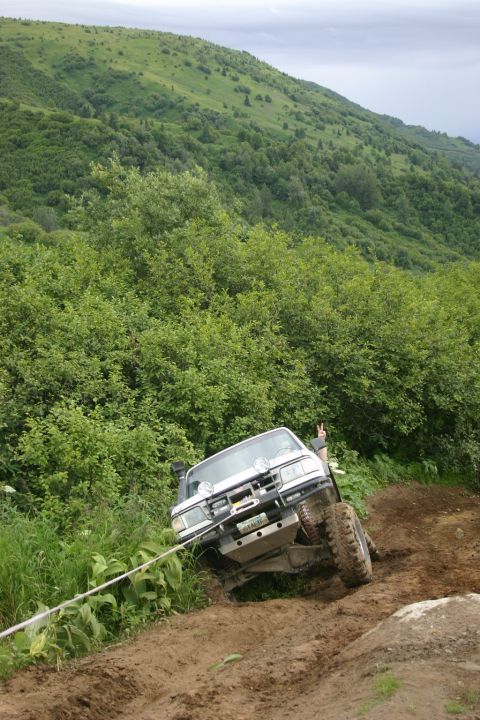 2003 Jeep TJ - A white 2003 Jeep TJ navigates a steep, muddy incline during an off-road excursion.