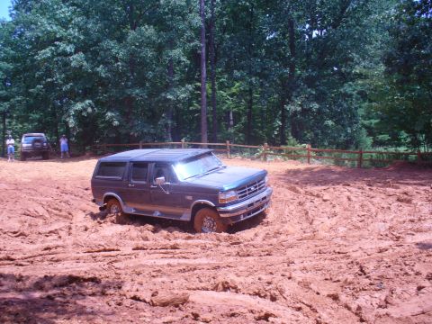 1996 Ford Bronco - A dark blue SUV navigates a challenging muddy terrain, with another vehicle visible in the background.