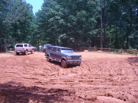 1996 Ford Bronco - Multiple 4x4s tackle a challenging mud pit during an off-road event.