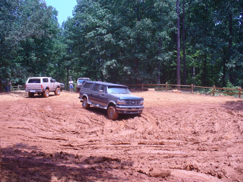 1996 Ford Bronco navigating a muddy off-road course with another Bronco and a pickup truck visible