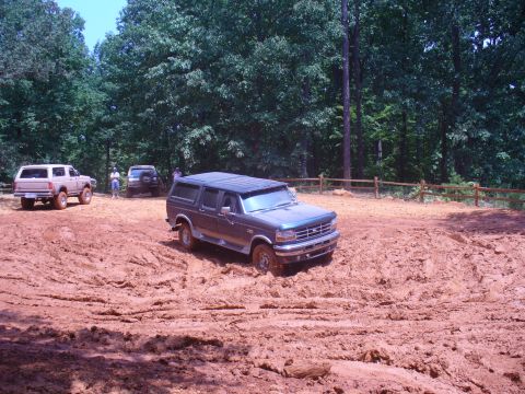 1996 Ford Bronco - Several vehicles navigate a muddy off-road course on a sunny day.