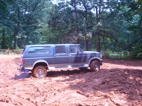 1996 Ford Bronco - Ford Bronco navigating a muddy off-road course surrounded by trees.